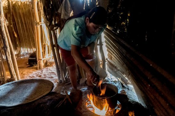 Eine Frau kocht am offenen Feuer in einer Hütte.