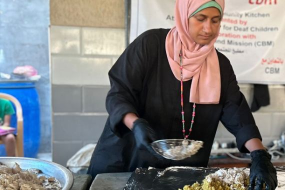 Eine junge Frau mit Kopftuch füllt ein Reisgericht von einem Blech in eine Schale.
