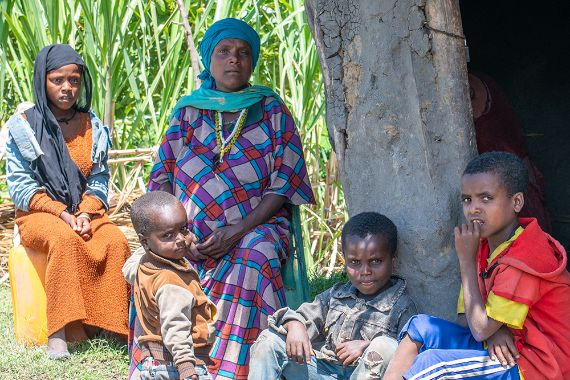 Eine Frau mit buntem Koptuch und geröteten Augen und vier Kinder sitzen vor einer Hütte.