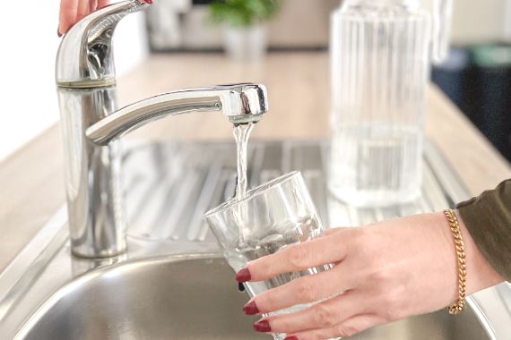 Ein Glas Wasser unter dem Wasserhahn wird aufgefüllt. 