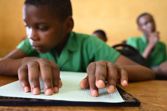 Ein Junge sitzt an einem Schreibtisch und liest von einer Braille-Tafel.