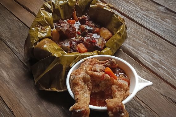 Ein mit einem Bananenblatt ausgelegtes Gefäß mit Gemüse-Fleisch-Ragout, daneben eine Schale mit Gemüse und Hühnerbeinen.