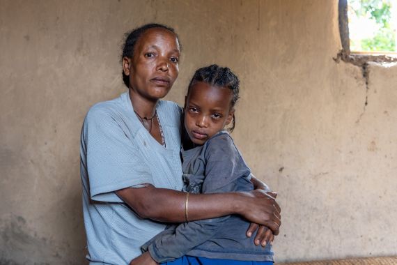 Eine Frau hält ein etwa fünfjähriges Mädchen mit kleinen, abstehenden Zöpfchen im Arm.