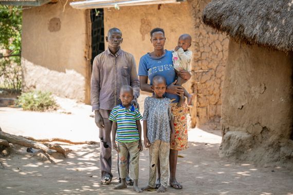 Eine Frau hält ein kleines Kind auf dem Arm, während sie neben einem Mann und zwei weiteren Kindern steht.