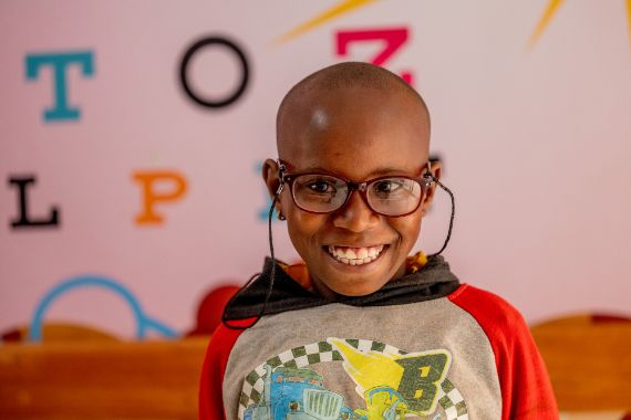 Ein siebenjähriges Mädchen trägt eine Brille mit einer Brillenkette. Sie lächelt.
