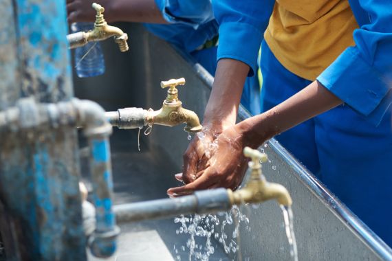 Aus Wasserhähnen über einer Wanne fließt Wasser. Zwei Personen halten die Hände in den Strahl.