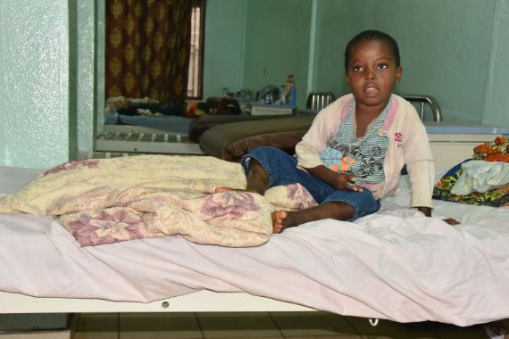 Kleines afrikanisches Mädchen sitzt auf einem Bett.