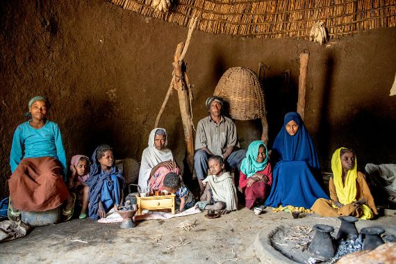 Eine zehnköpfige Familie sitzt in einer Hütte um eine Feuerstelle. 