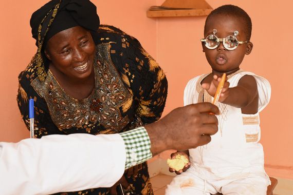 Kleiner afrikanischer Junge mit Refraktionsbrille greift nach einem Stift.