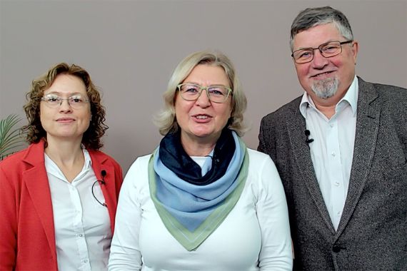 Zwei Frauen und ein Mann stehen nebeneinander. Sie lächeln.