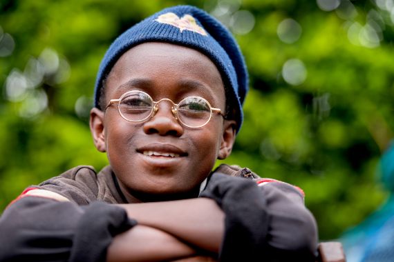 Lächelndes afrikanisches Kind mit Brille und Mütze.