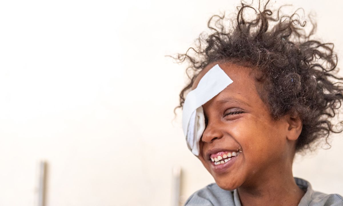 Lachendes, lockenköpfiges Kind mit Augenverband