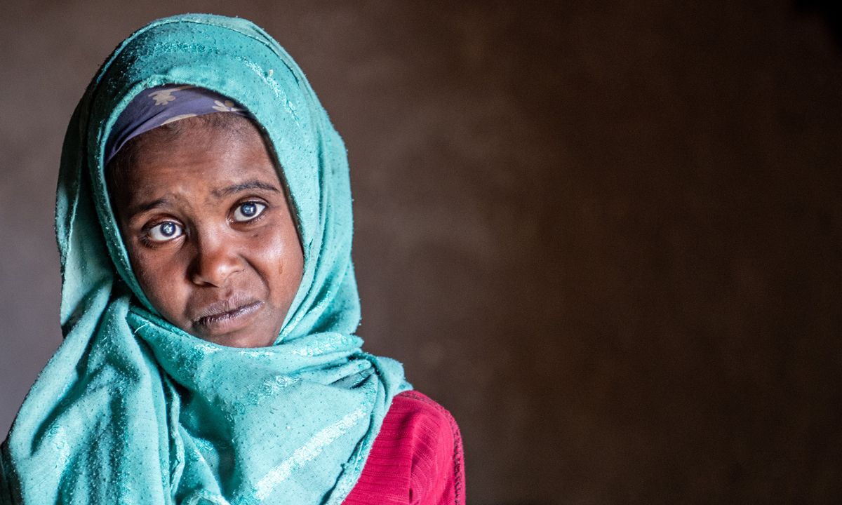 Etwa neujähriges Mädchen mit leuchtend türkisfarbenen Kopftuch hat auffallend weiße Pupillen.