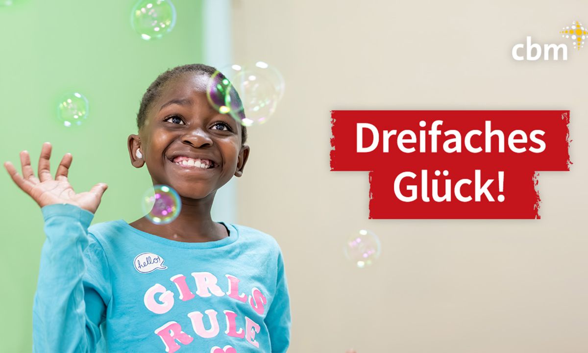 Ein etwa zehnjähriges, lachendes Mädchen greift nach Seifenblasen. Schrift auf einem roten Balken: Dreifaches Glück!