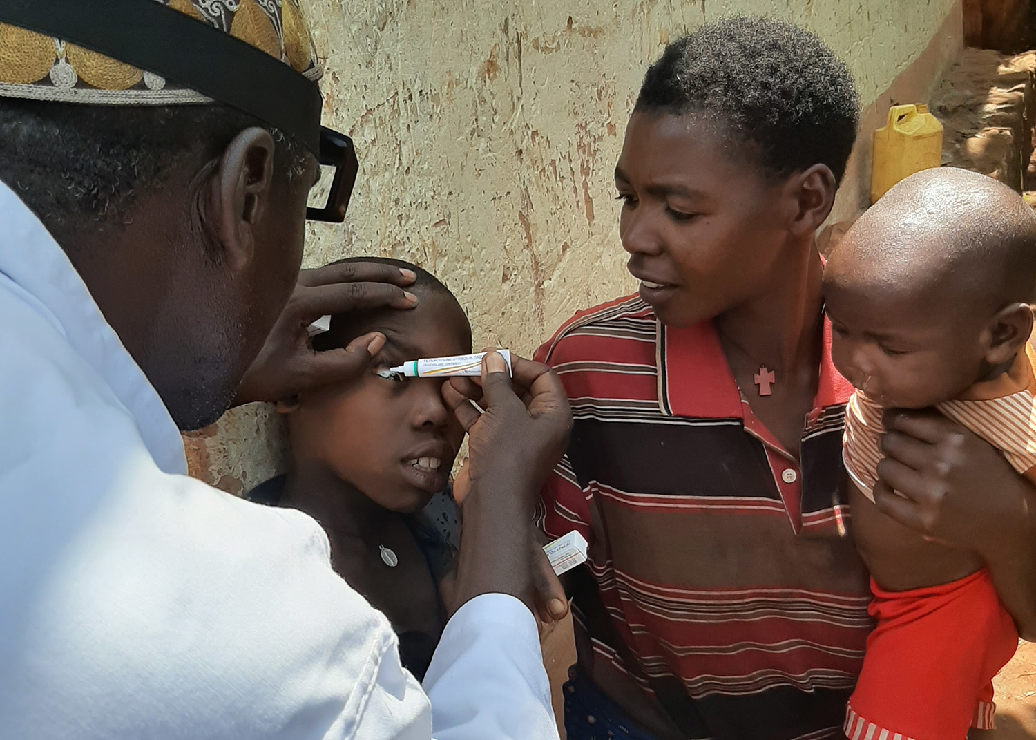 Ein Mann behandelt das Auge eines Kindes mit Salbe.